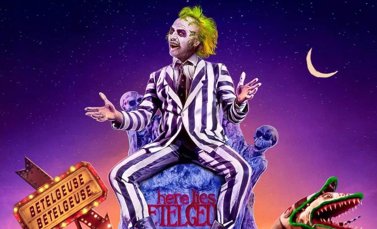 michael keaton como bitelchús , subido encima de una lápida en un cementerio con un fondo naranja y lila